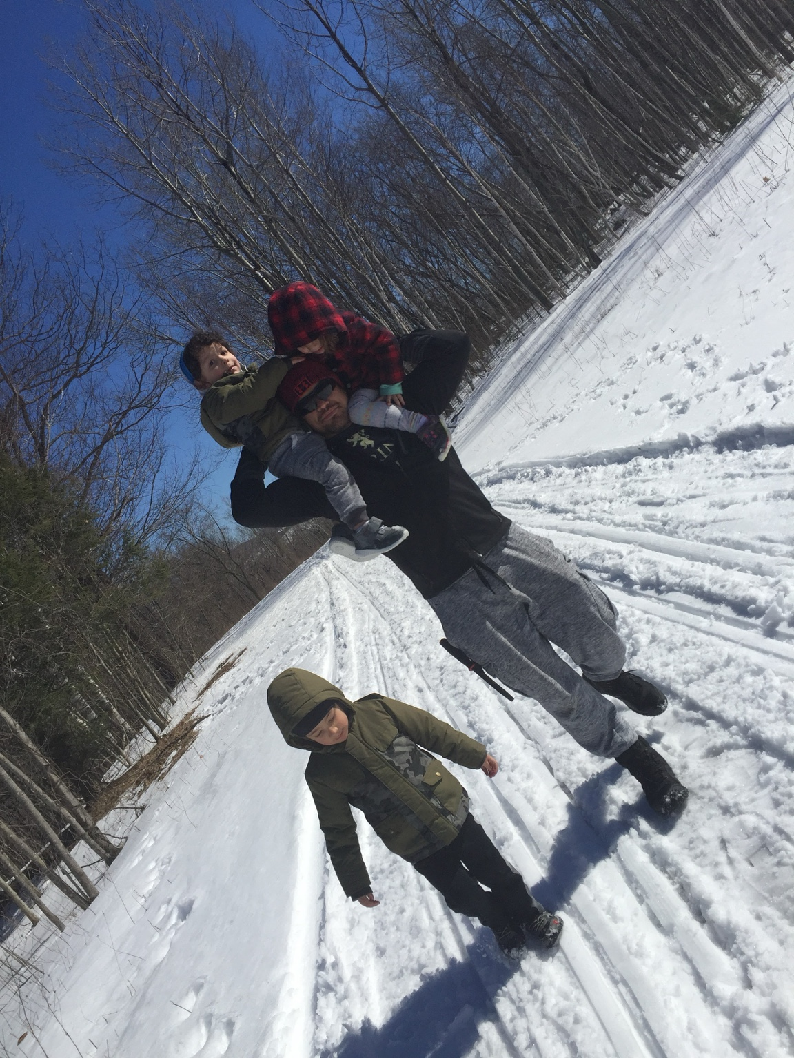 Romulo carrying two of his children while another walks beside him on a snowy winter trail